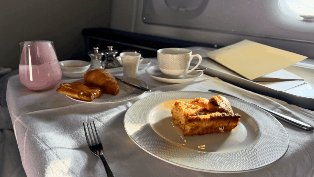 British Airways First Class Breakfast Inflight Meal | Journey Beyond 40 inflight first class breakfast on british airways featuring a berry smoothie, a baked frittata, a croissant, and a danish pastry served on white tableware.
